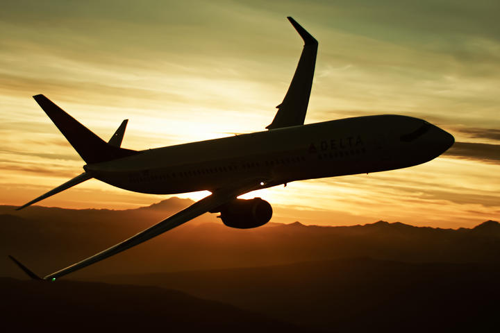 A 737-900 flies with a sunset in the background, creating a silhouette of the aircraft.