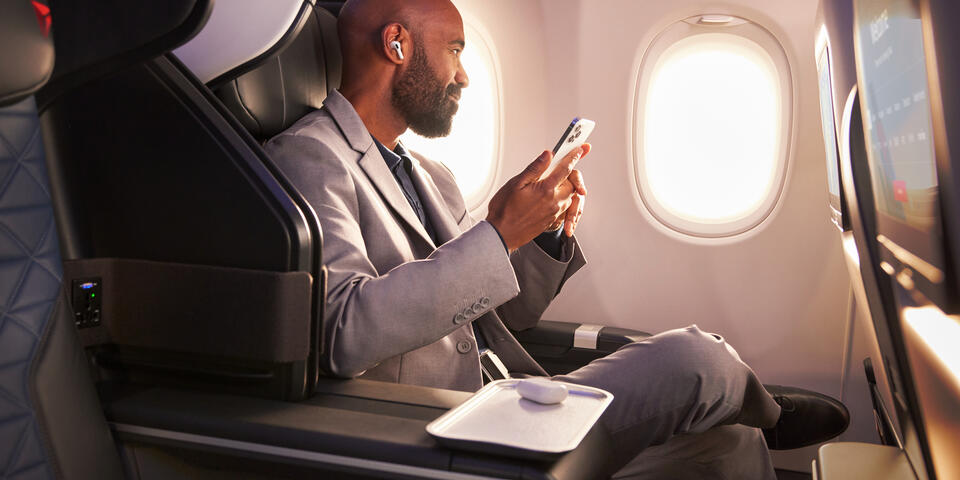 A Delta customer sits in Delta's First Class cabin, holding their phone.