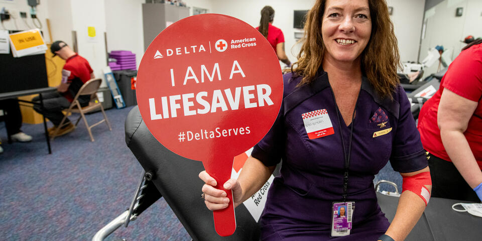A Delta employee holds up a sign that says "I am a lifesaver" while giving blood.